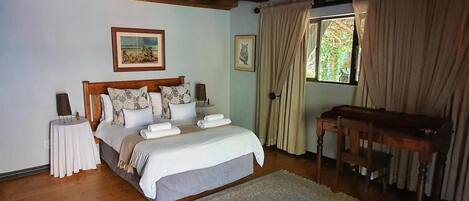 A bedroom with a wooden ceiling, a bed with white bedding, a nightstand, a table, and a window with curtains.