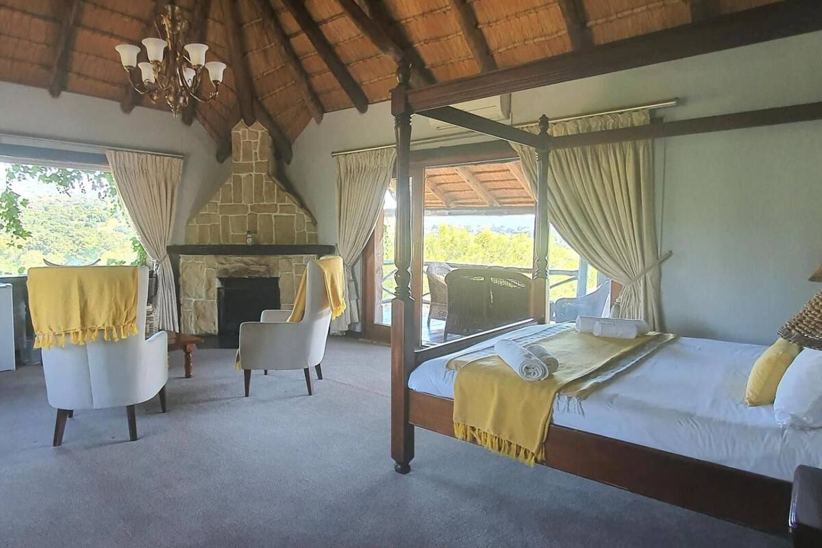 Una habitación con una cama con dosel, una chimenea de piedra, dos sillones y una araña.