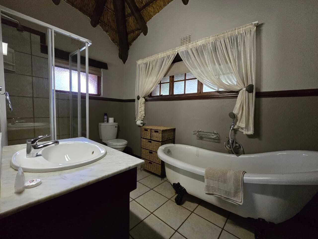 A bathroom with two sinks, a bathtub, a window with curtains, and a wicker basket.