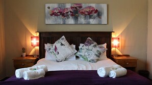 Un lit bien fait, agrémenté d’oreillers à motifs floraux, d’un plaid violet et de deux lampes de chevet.