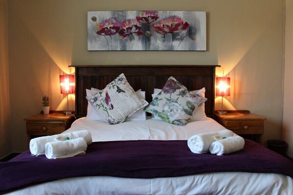 A neatly made bed with floral pillows, a purple throw blanket, and two bedside lamps.