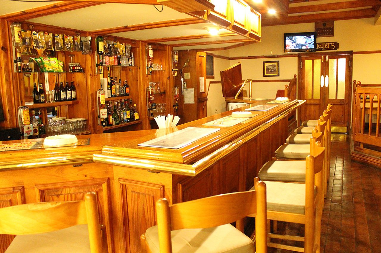 A bar area with wooden furniture, a television, and various bottles and glasses on shelves.