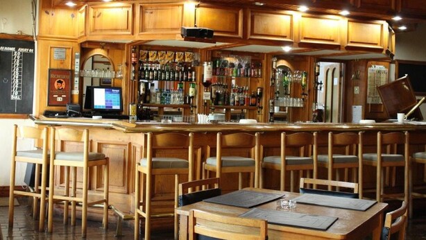 Un espace bar avec des meubles en bois, un comptoir équipé d’un ordinateur et des étagères remplies de bouteilles.