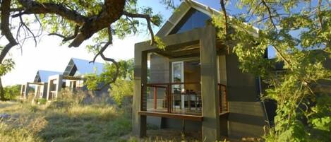 Eine moderne, gläserne Hütte mit Balkon, umgeben von natürlicher Vegetation und ähnlichen Bauten.