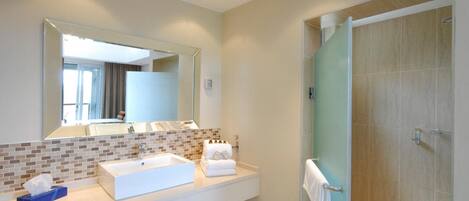 Un baño moderno con un espejo grande, un lavabo blanco y una ducha con mampara de vidrio.