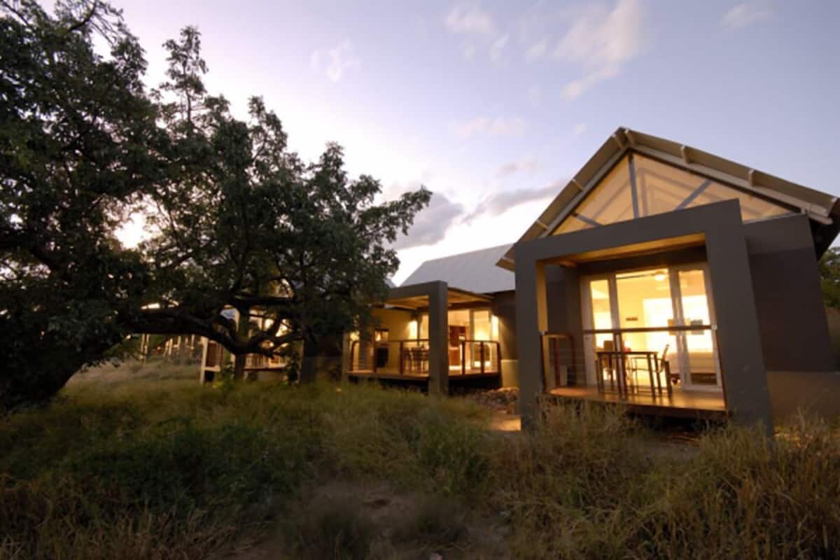 A modern house with large windows and a covered porch, surrounded by trees and grass.