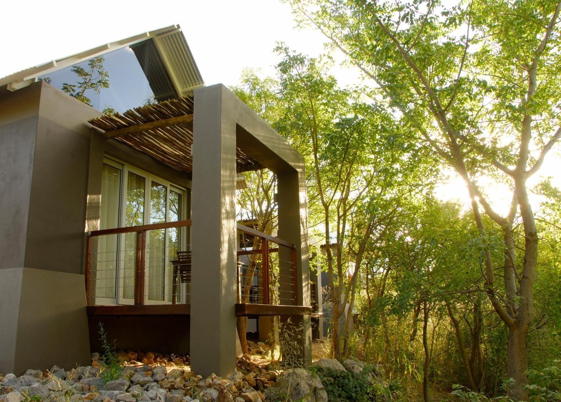 Un edificio moderno con amplios ventanales, una terraza de madera y un paisaje natural circundante.