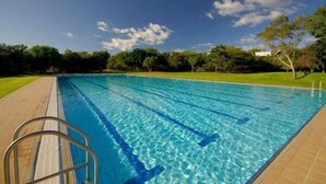A clear swimming pool with lane dividers, surrounded by a grassy area and trees under a partly cloudy sky. - Kupferquelle Resort (Tsumeb)