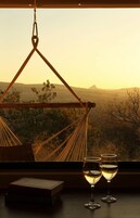 Uma rede com vista para uma paisagem desértica, dois copos de vinho branco e um livro sobre uma mesa.