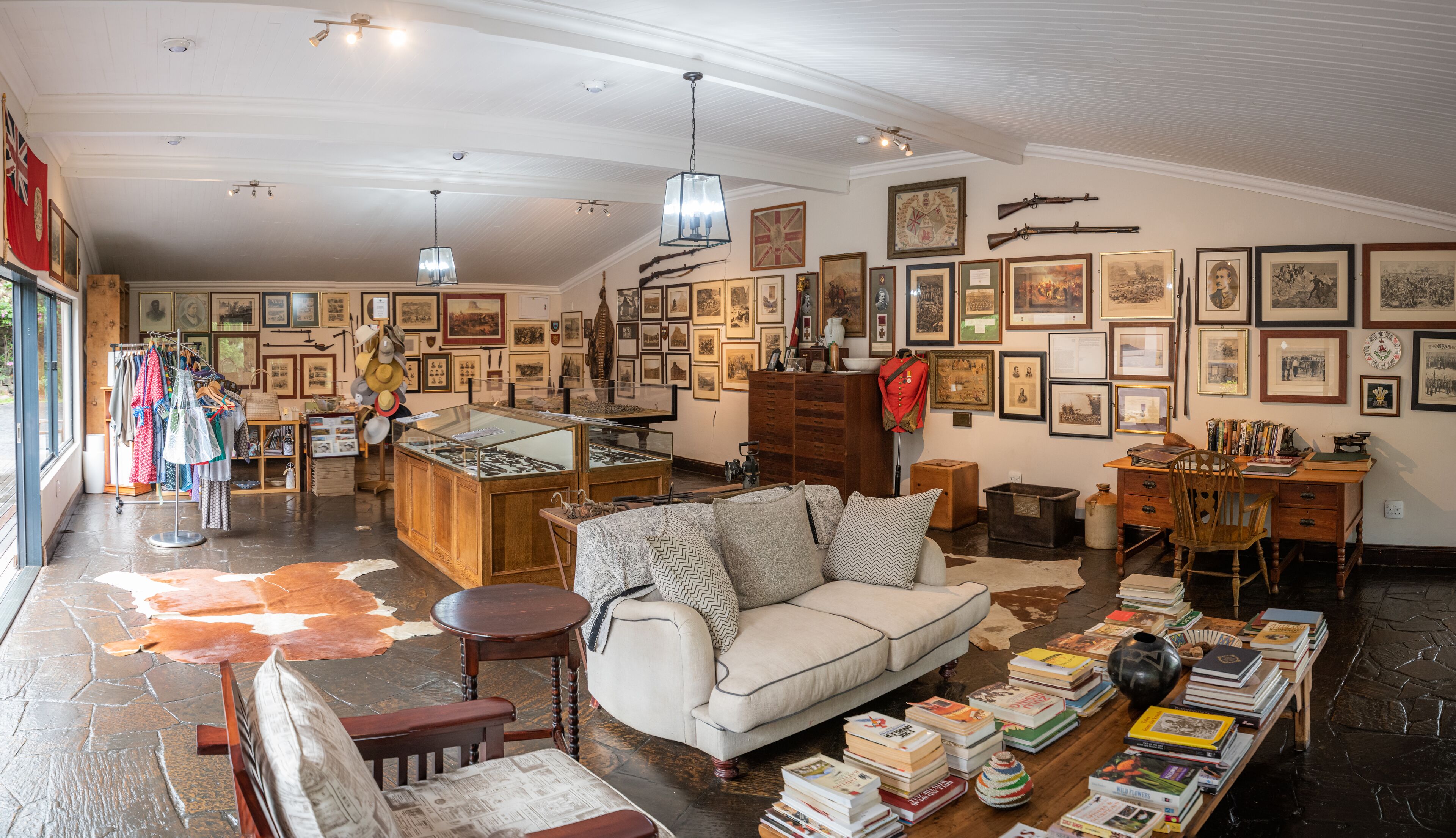 Una habitación amplia con un sofá grande, un escritorio de madera y una variedad de libros y objetos expuestos en las paredes.