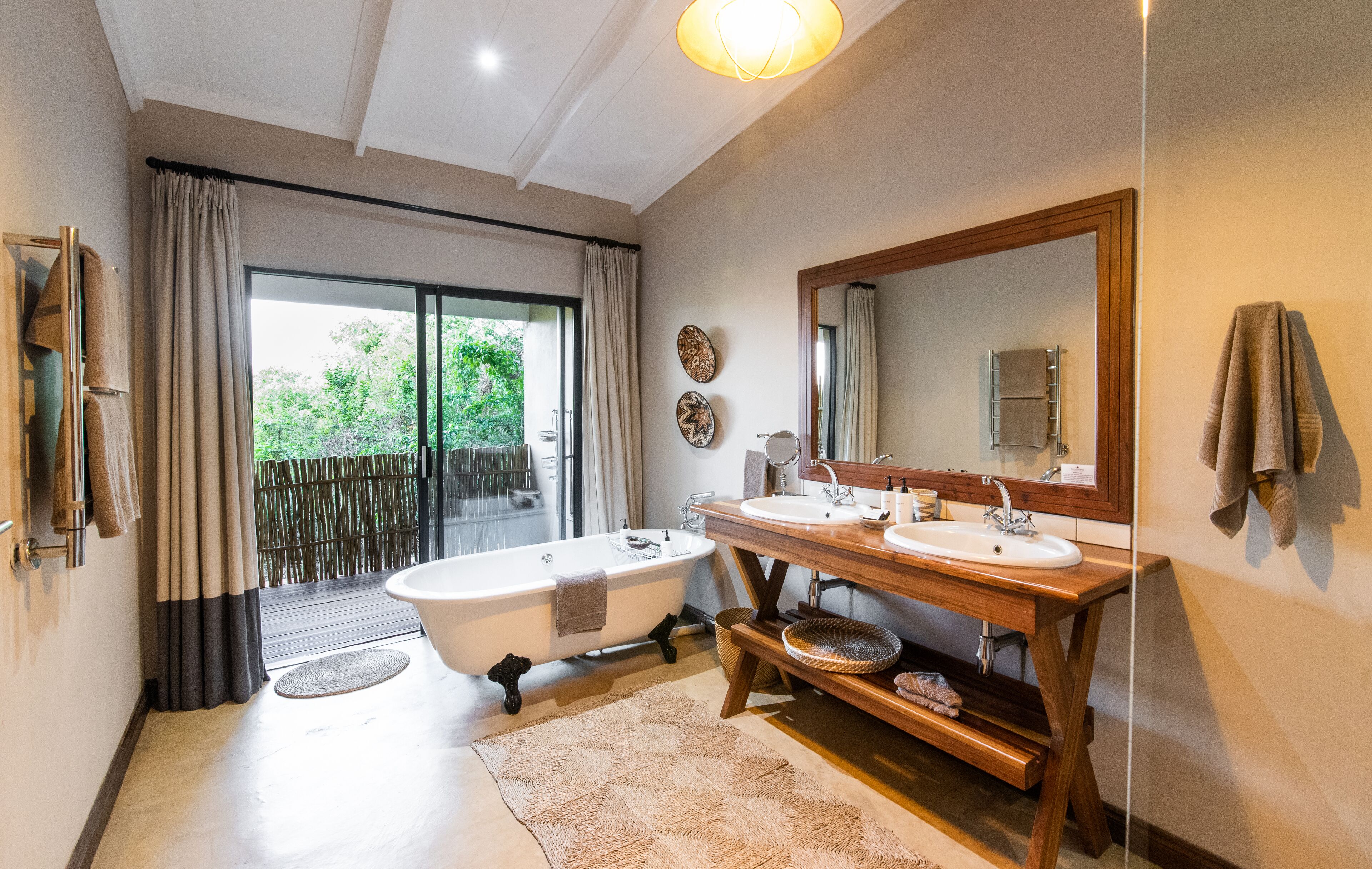 A modern bathroom with a bathtub, two sinks, a large mirror, and a sliding glass door leading to a balcony.