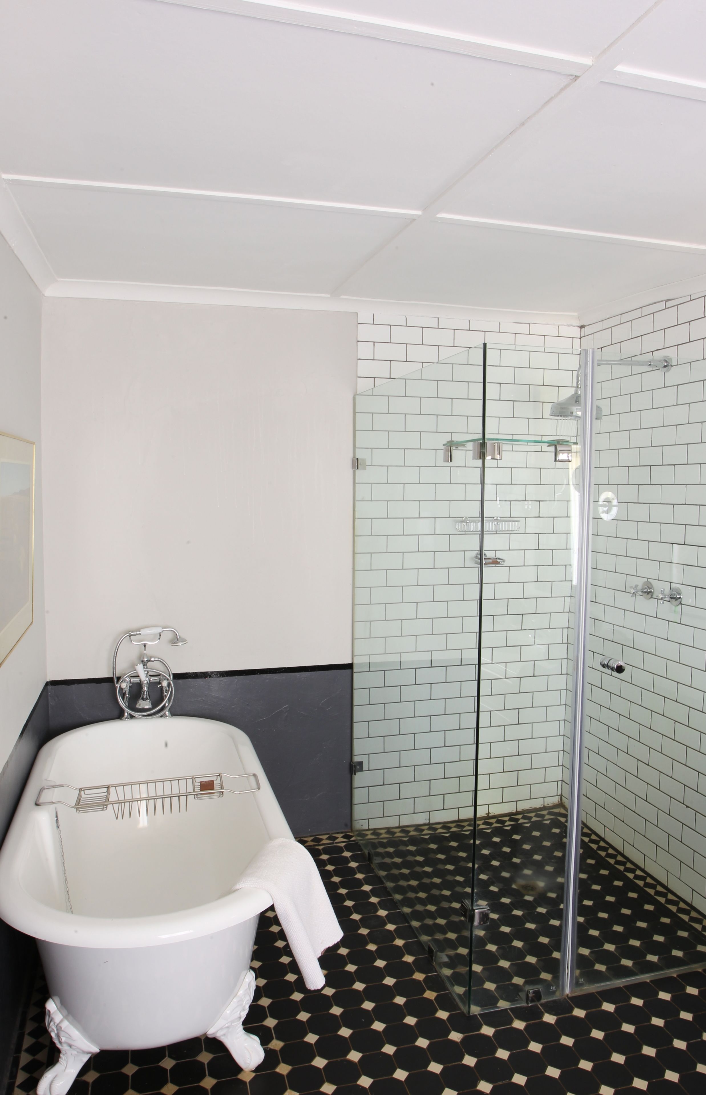Une salle de bain avec une baignoire blanche, une douche à parois de verre et un carrelage noir et blanc à motifs carrés.