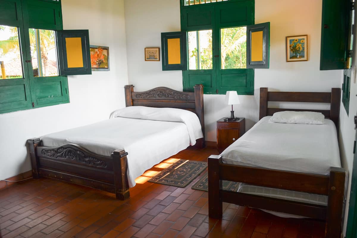 A room with two wooden beds, a nightstand, and a window with green shutters.