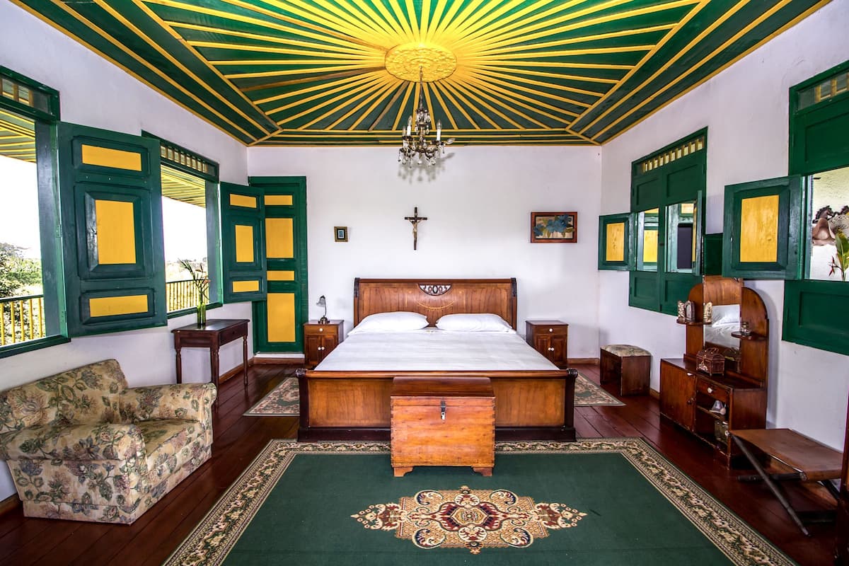 A room with a large bed, a wooden chest, a chair, and a chandelier.