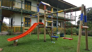 A playground with a slide and swings, set against a building with a balcony and a yellow railing. - Finca Hotel El Palmar (Montenegro)