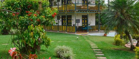 A two-story building with a tiled roof, a balcony on the upper floor, and a well-maintained lawn with stepping stones leading to the entrance.