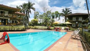 A swimming pool with lounge chairs and umbrellas, surrounded by a landscaped garden and two-story buildings. - Finca Hotel El Palmar (Montenegro)