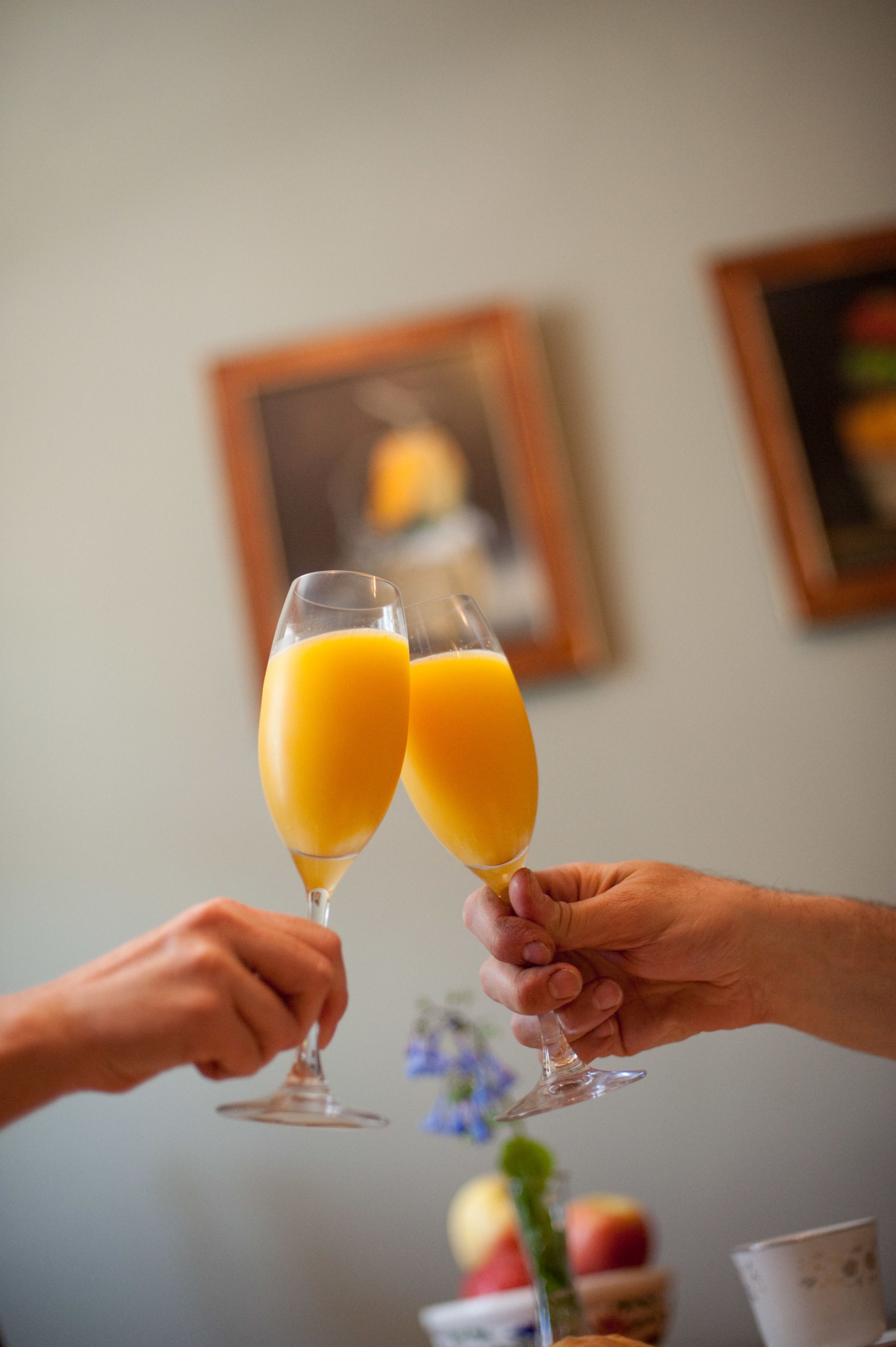 Deux mains tenant des coupes à champagne remplies de jus d’orange.
