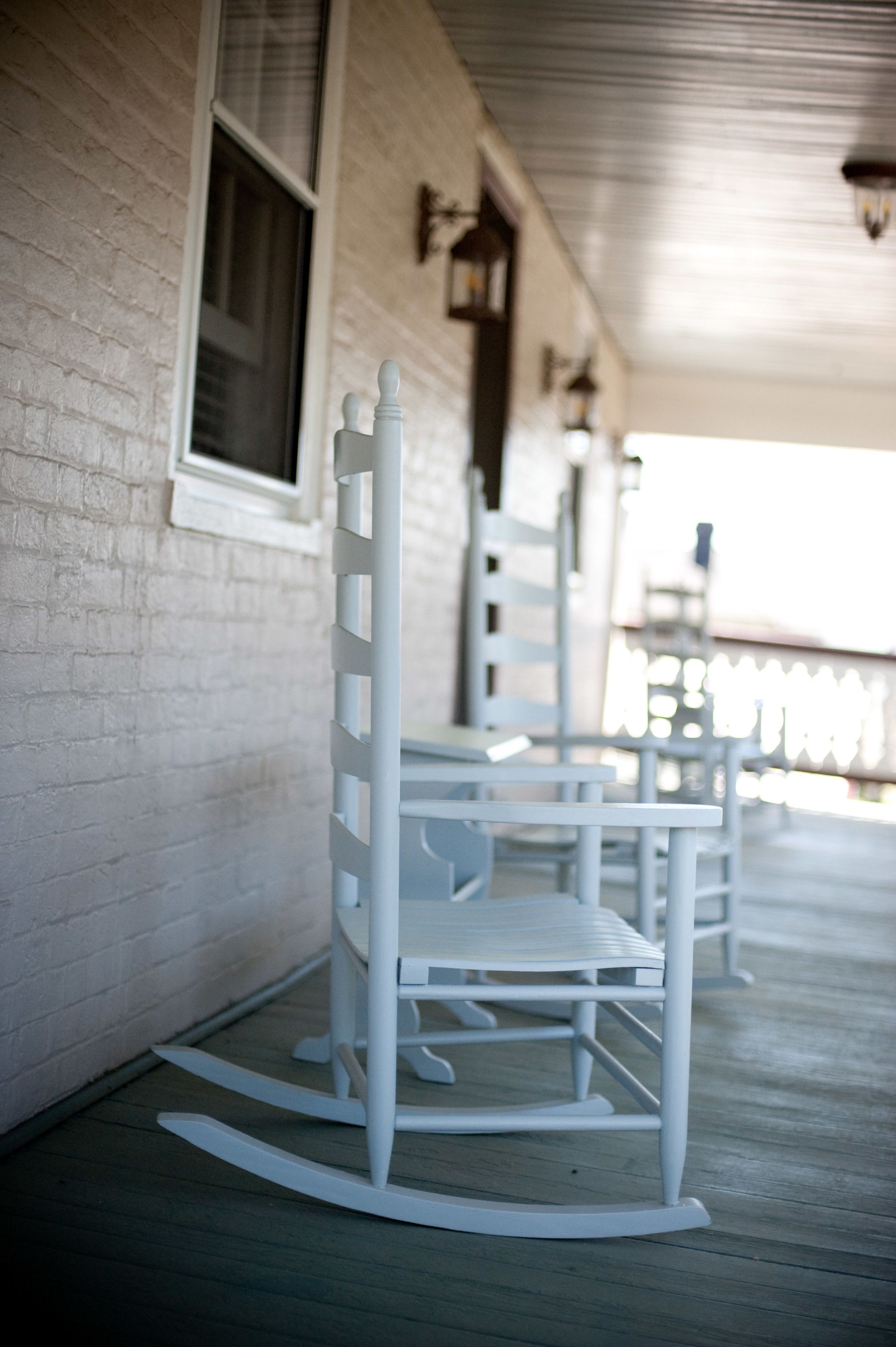 Rocking chairs on a porch with a white brick wall and windows.