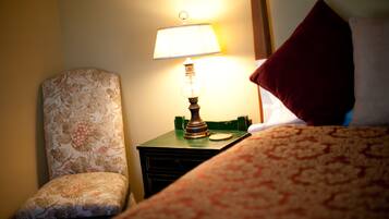 Una habitación de hotel con un sillón estampado de flores, una mesita de noche con una lámpara y una cama con colcha estampada.