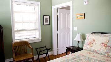 Une chambre à coucher comprenant un lit, une chaise, une table de chevet, une lampe, une fenêtre avec des stores et une porte.