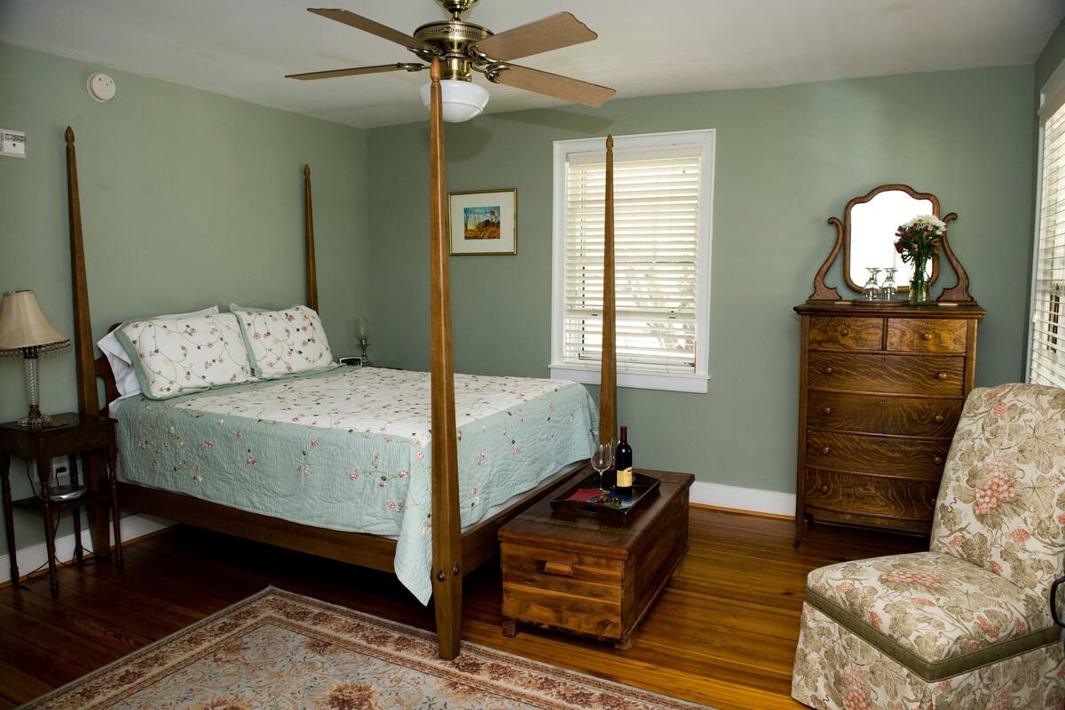 Ein Schlafzimmer mit einem Himmelbett, einer Holzkommode, einem Sessel und einem Deckenventilator.