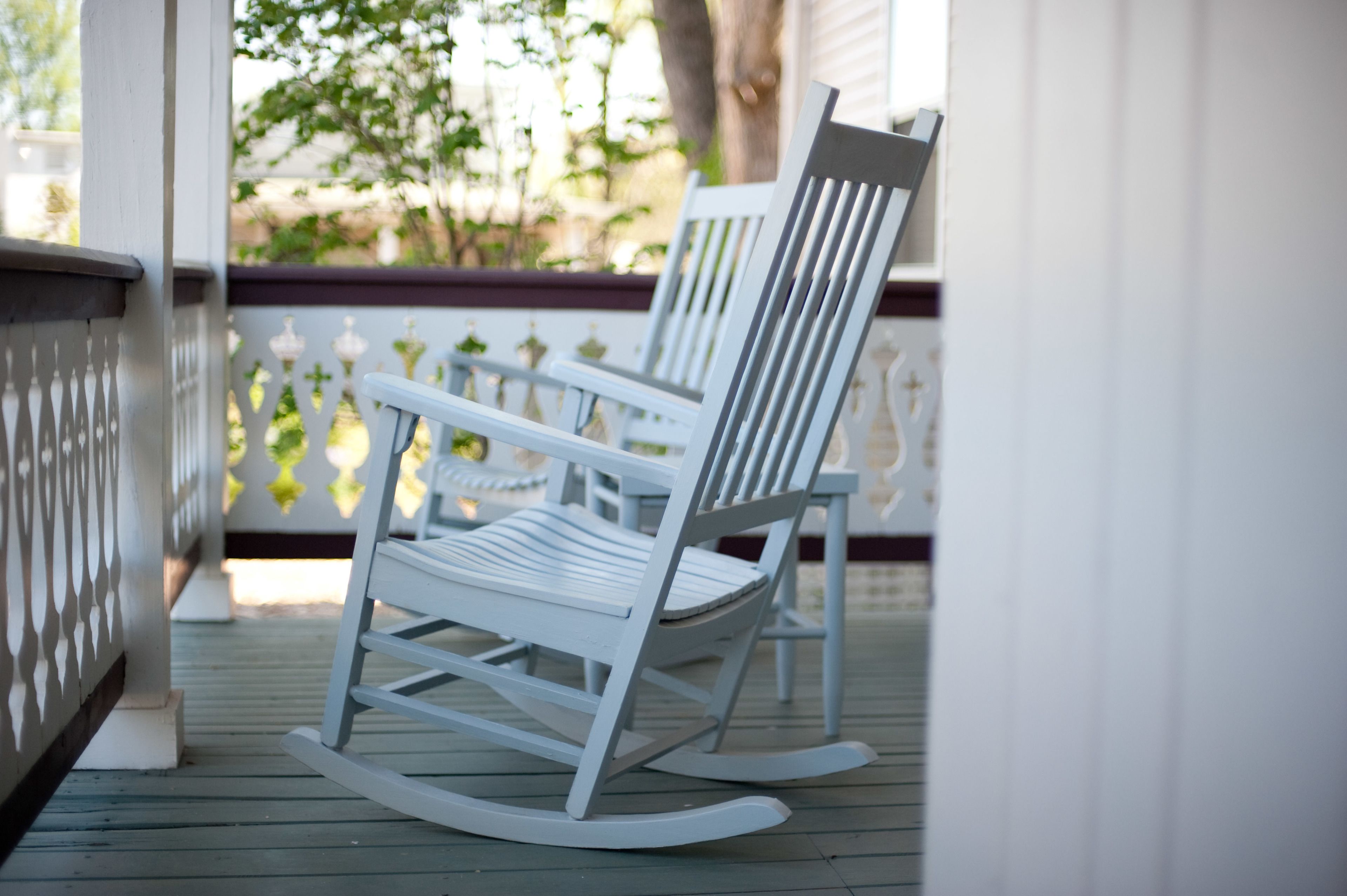 A white rocking chair on a wooden deck with a white railing and decorative posts.
