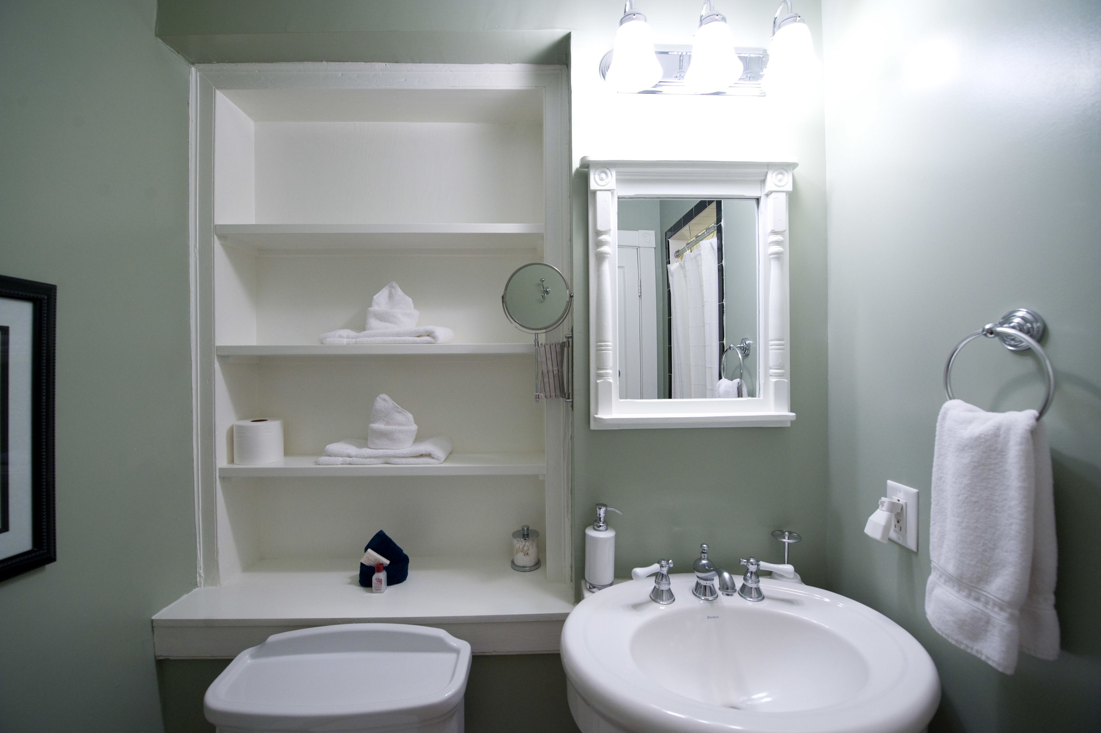 A bathroom with a white sink, a mirror, shelves with towels, and a toilet.