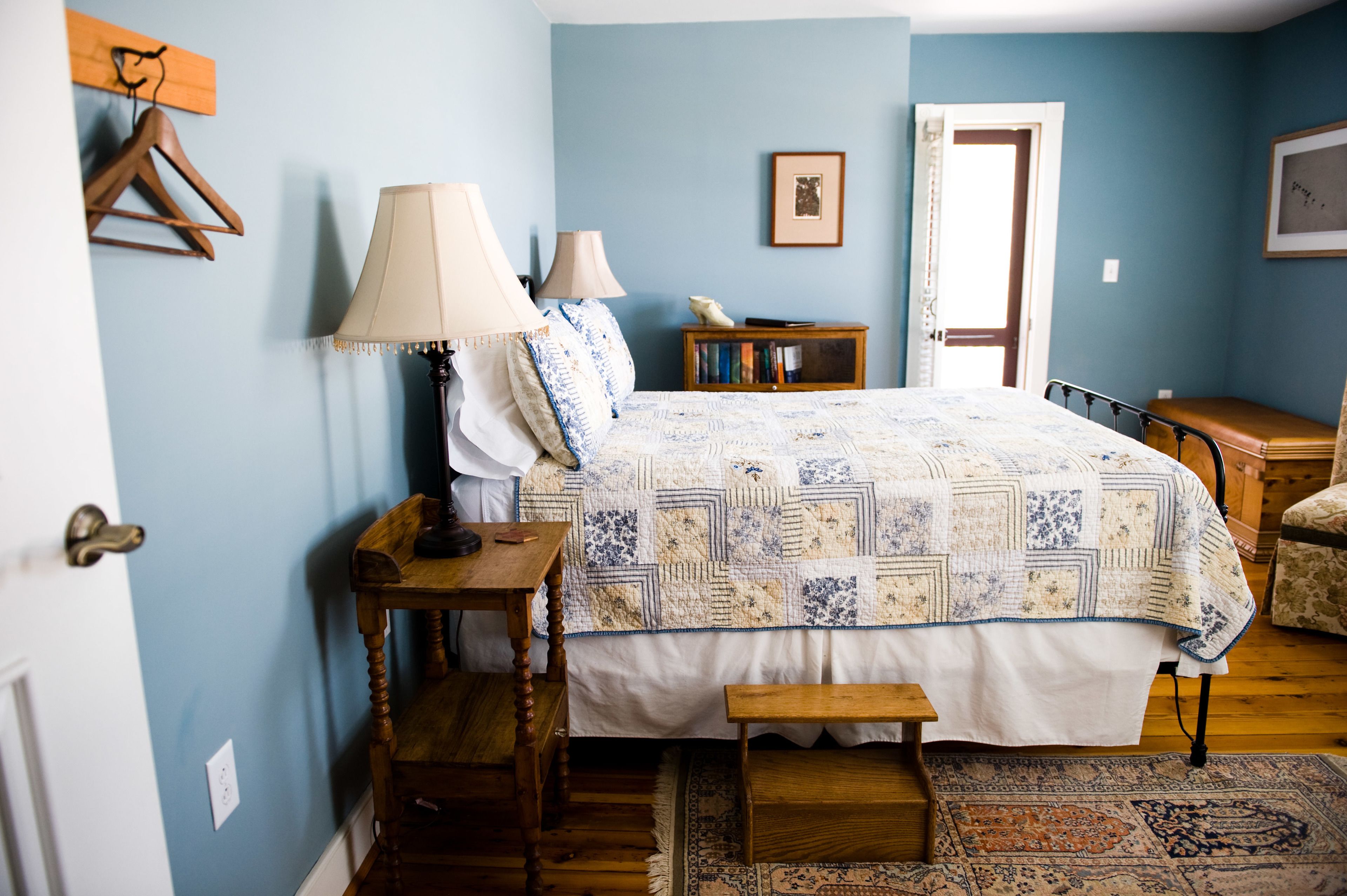 A bedroom with a bed, two bedside tables, a wooden bench, a nightstand, a bookshelf, and a door.