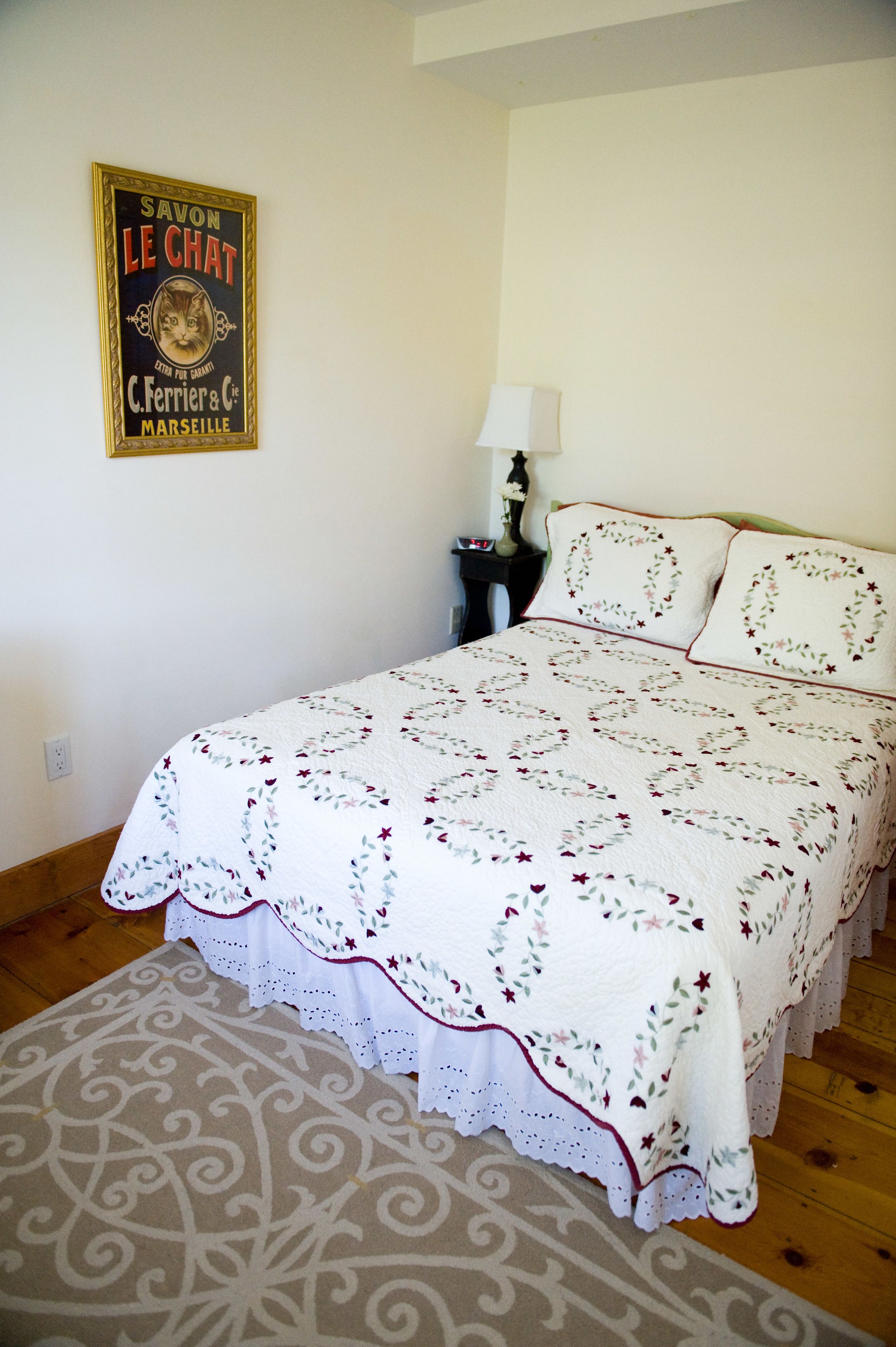 Een opgemaakt bed met een bloemenprint, een klein nachtkastje met een lamp en een poster aan de muur.