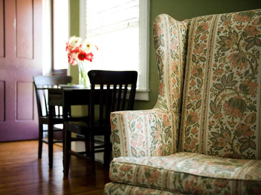 Une pièce avec un canapé à motifs floraux, une table à manger en bois et des chaises, et une porte violette.