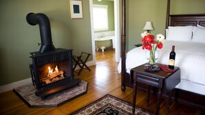 A room with a wood-burning stove, a bed, a nightstand with a vase of flowers, and a bedside table with a bottle and glasses. - Hopkins Ordinary Bed Breakfast and Ale Works (Sperryville)