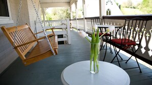 A porch with a swing chair, a table with a vase of flowers, and outdoor seating. - Hopkins Ordinary Bed Breakfast and Ale Works (Sperryville)