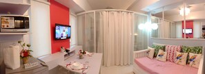 A hotel room with a television, a microwave, a bed with decorative pillows, a bedside table with a vase of flowers, and a curtain. - HomeStay at Wind Residences (Tagaytay)