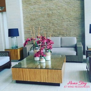 A modern living room with a glass coffee table, a grey sofa, and wicker chairs. There are decorative jars with pink flowers on the table. - HomeStay at Wind Residences (Tagaytay)