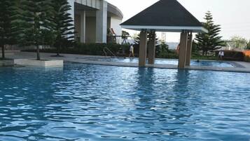 A swimming pool with a gazebo, surrounded by trees and a building.