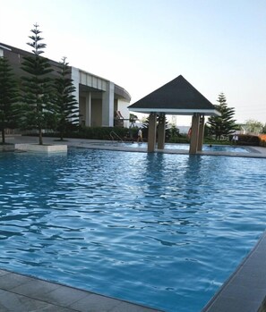 A swimming pool with a gazebo, surrounded by trees and a building. - HomeStay at Wind Residences (Tagaytay)