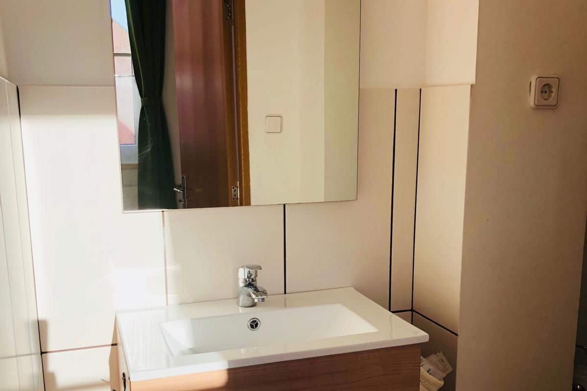 A bathroom with a white sink, wooden vanity, and a mirror above the sink.