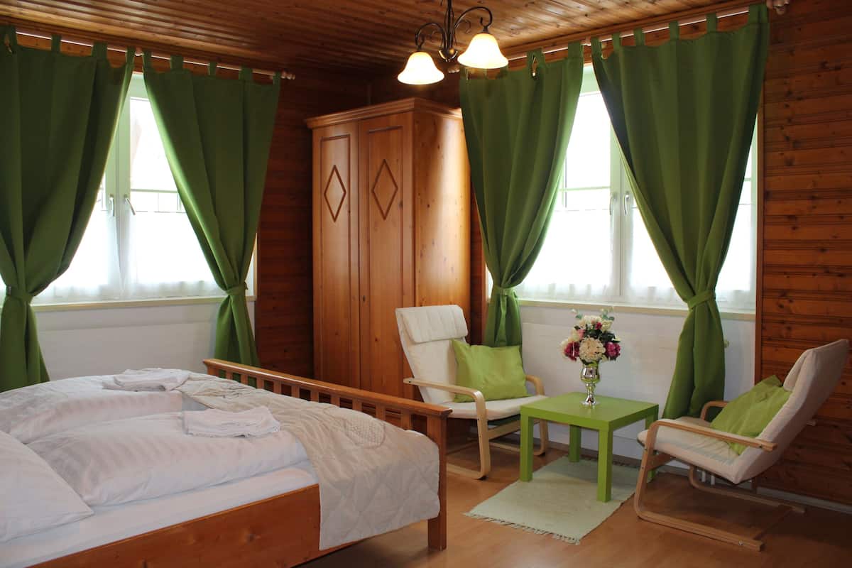 A wooden cabin room with a bed, two chairs, a table, and a cabinet.