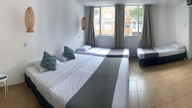 Habitación de hotel con una cama grande, otra más pequeña, una ventana con cortinas, una lámpara colgante y un taburete.