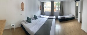 A hotel room with a large bed, a smaller bed, a window with curtains, a hanging light fixture, and a small stool. - Hotel Quintas de Normandia (Bogotá)