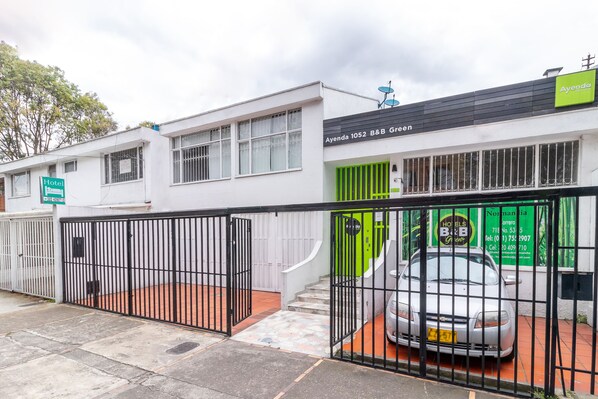 A hotel with a white exterior, a green door, and a black gate. - Hotel Quintas de Normandia (Bogotá)