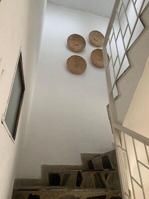 Uma escadaria com uma parede branca e uma janela à esquerda, que leva a um patamar.