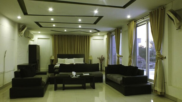 A modern living room with a large bed, a sofa, a coffee table, and a TV. - Capetown Guest House (Islamabad)