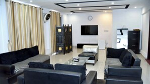 A modern living room with black sofas, a glass coffee table, a flat-screen TV, and a black cabinet. - Capetown Guest House (Islamabad)