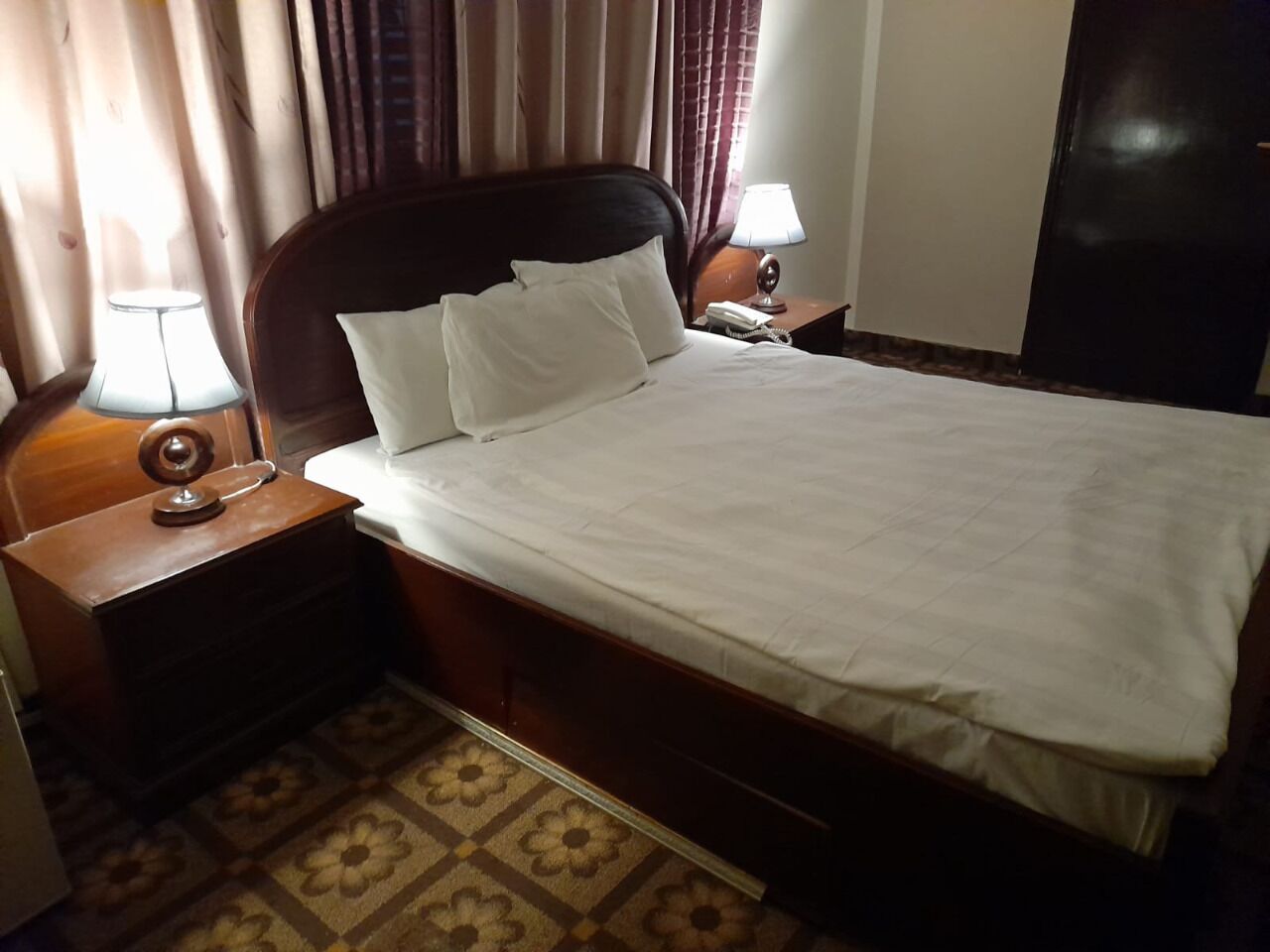A hotel room with a bed, two bedside tables, a lamp, and a telephone.