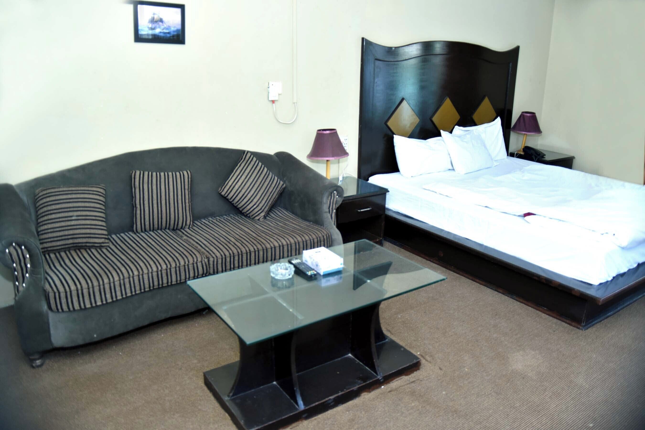 Una habitación de hotel con una cama, un sofá, una mesa de centro de vidrio y dos lámparas de noche.