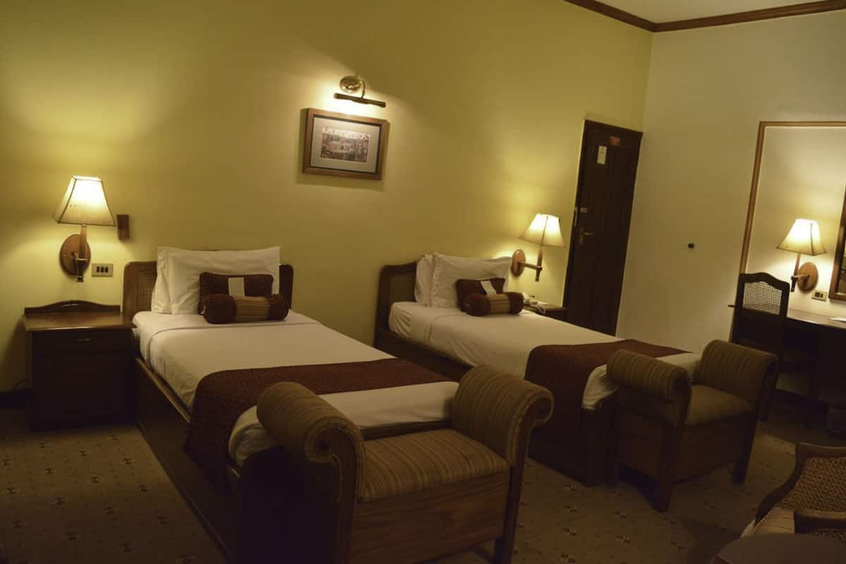 A hotel room with two beds, a desk, a chair, and a mirror.