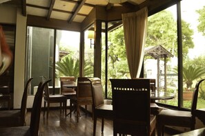 A dining area with wooden furniture and large windows offering a view of greenery outside. - Chateau Royal (Islamabad)