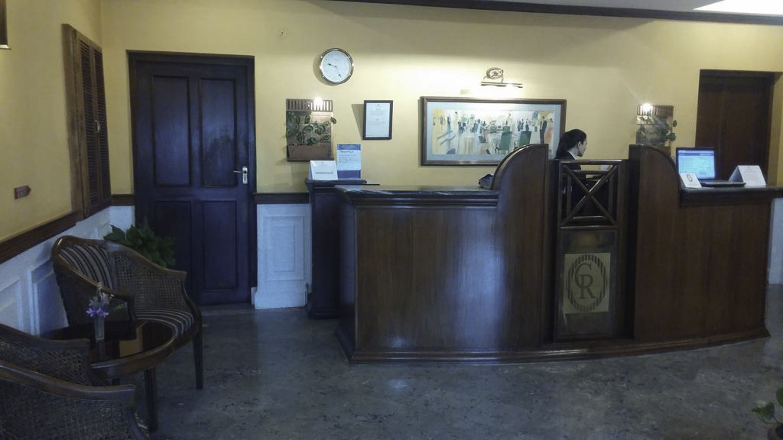 A reception area with a wooden reception desk, a clock, framed artwork, and a seating area with wicker chairs.